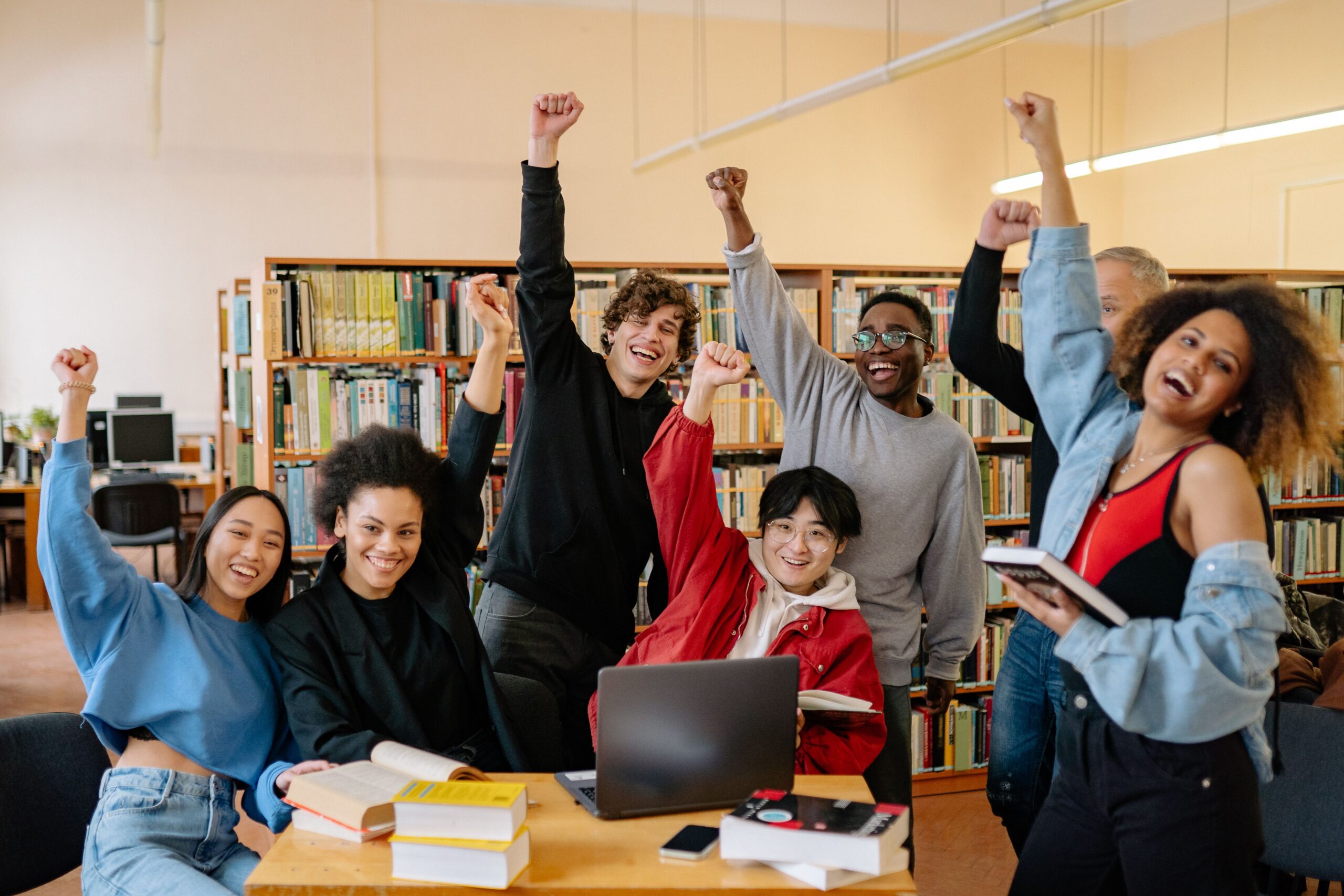 Groupe d'étudiants célébrant dans une bibliothèque, bras levés.