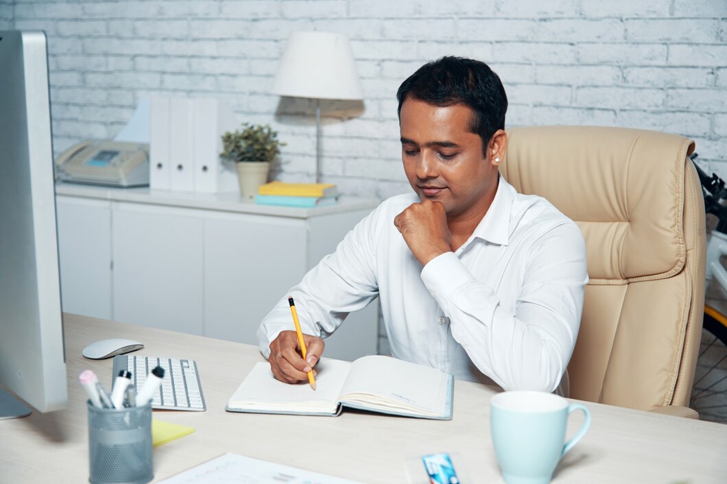 Homme écrivant dans un carnet à un bureau moderne.