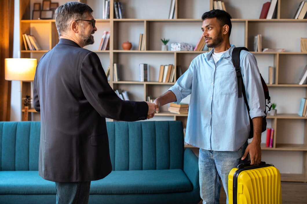 Deux hommes se serrent la main dans un salon, valise jaune à côté.